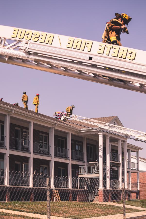 A firefighter descends from the roof of Burrage大厅 on the ladder of one of 克里特岛 Volunteer Fire Department's trucks. Other firefighters practice cutting ventilation holes in the roof of the residence hall, which will be demolished later this summer. 